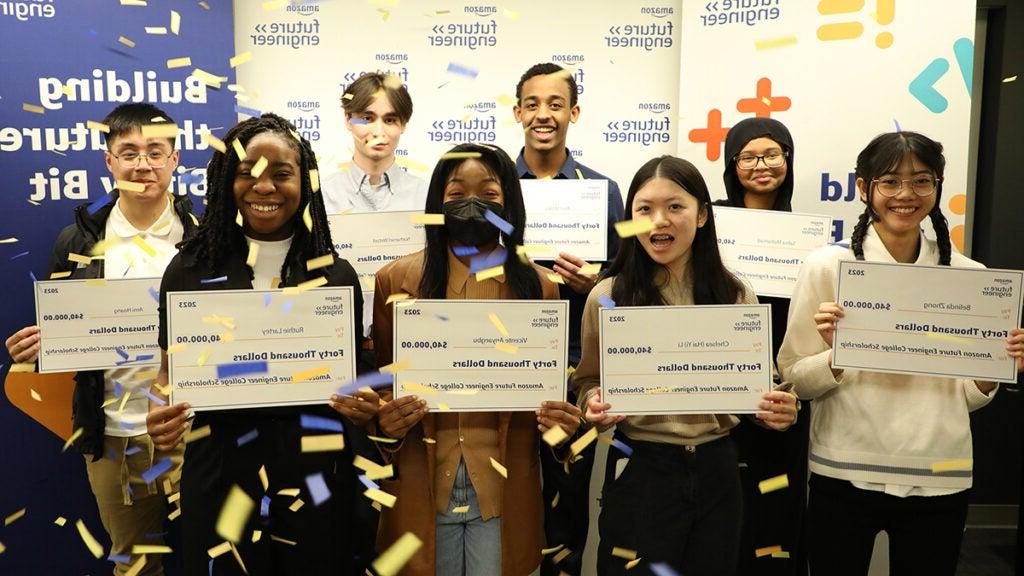 A group of eight students hold large checks while confetti falls on them